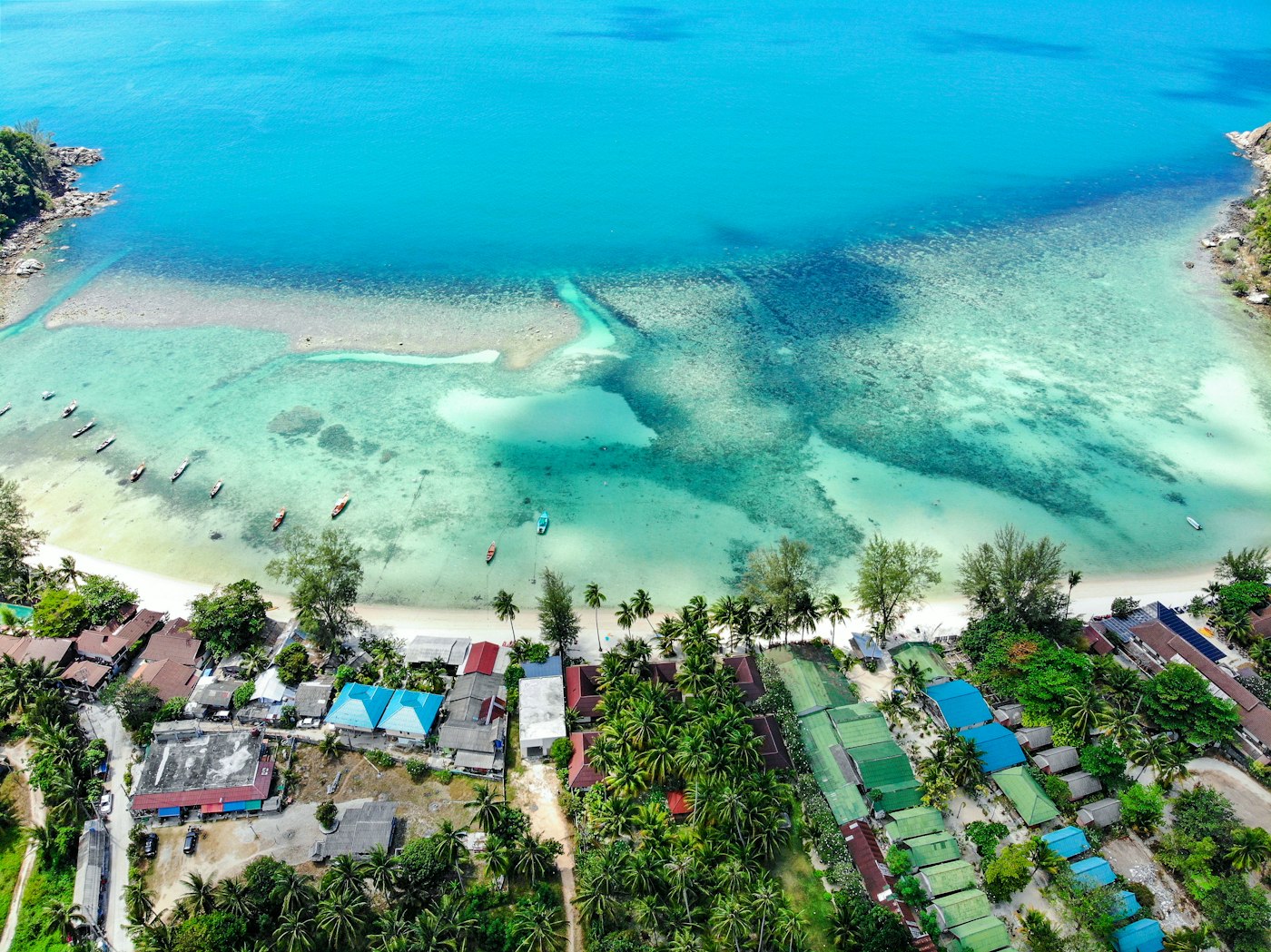 Aerial view of a shallow reef bay on the north coast of Koh Phangan, with longtail boats moored above a pale sandbar